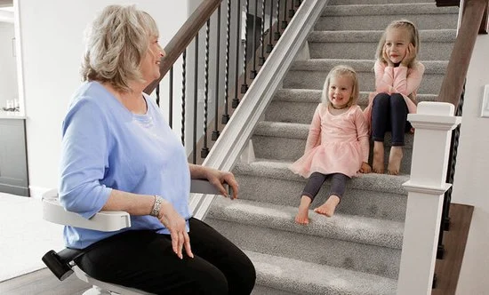 a woman riding an indoor stair lift with kids sitting on the steps watching