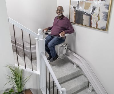Man riding a Bruno Elite curved stairlift down a staircase with a landing