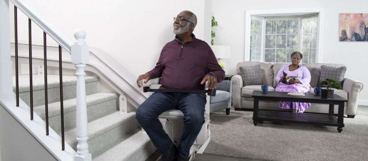 Man riding a Bruno Elite curved indoor stairlift up a flight of stairs after having service work performed