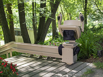 Bruno Elite curved outdoor stairlift parked and folded at the top of a wooden staircase in the woods
