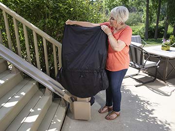 Woman placing a black all-weather cover for Bruno Elite straight outdoor stairlifts on top of a unit