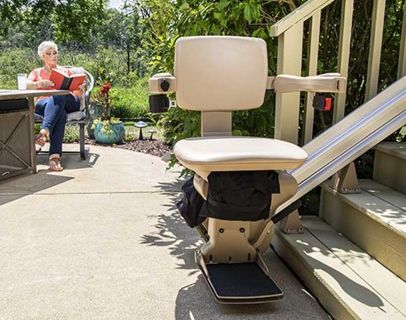 Bruno Elite straight outdoor stairlift parked on deck steps with a woman in the background to show how stairlifts helps people enjoy the outdoors